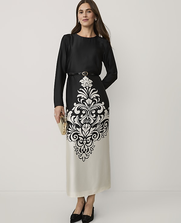 A woman wearing a black and white patterned dress and black heels stands against a plain white background.