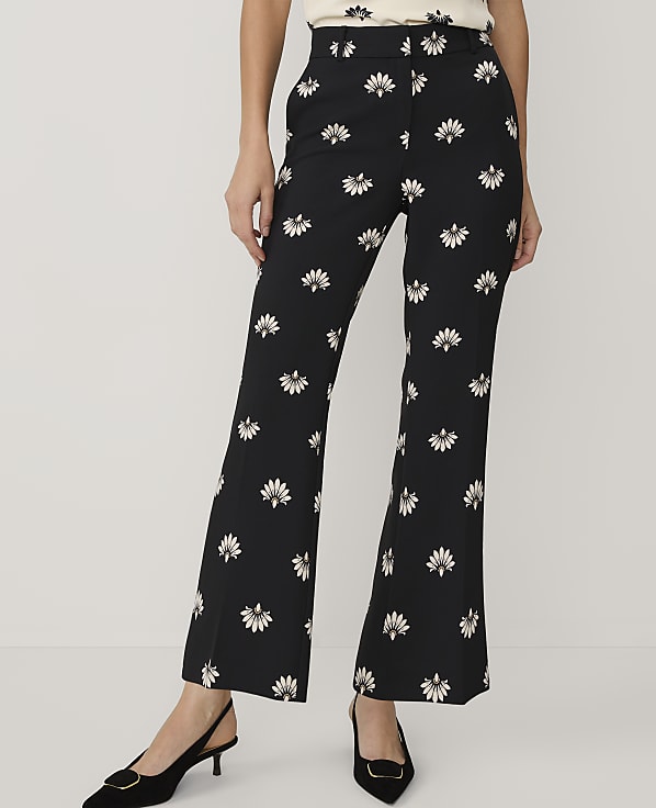 A person wears black floral-print trousers and black pointed-toe heels against a plain white background.