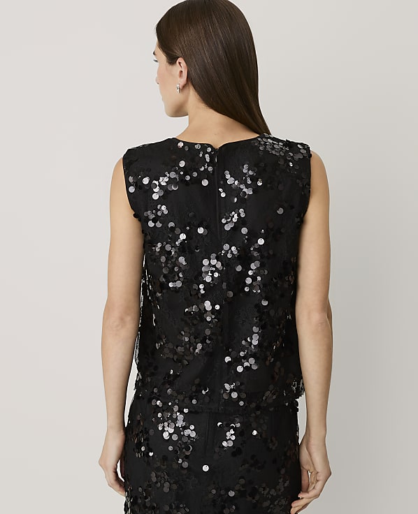 A woman with long brown hair stands with her back to the camera wearing a black sequined top and skirt against a plain light gray background.