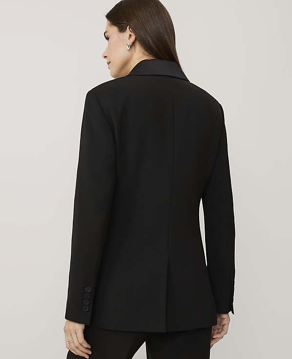 A woman wearing a black blazer is seen from behind against a plain, light-colored background.