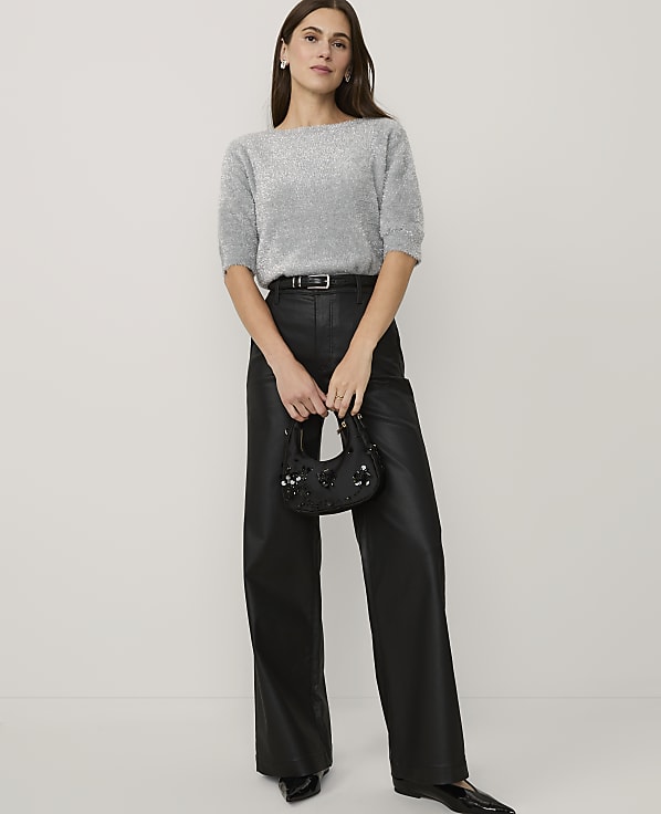 A woman wearing a shimmering silver top and black faux-leather trousers stands against a plain white background.