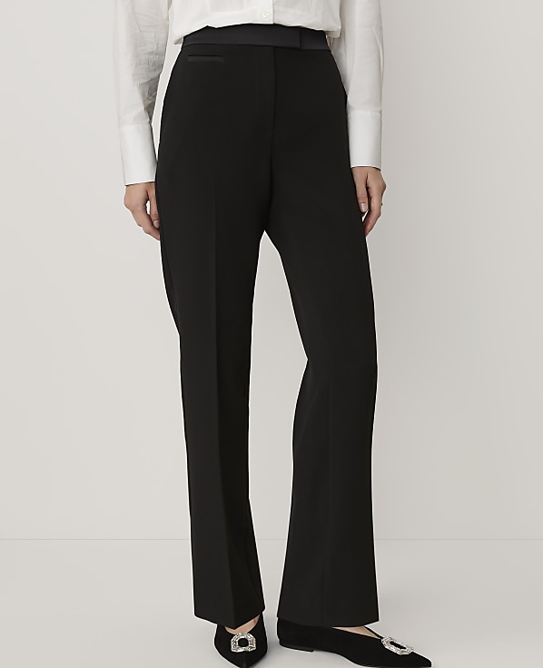 A person wears a white button-down shirt and black trousers with embellished shoes against a plain white background.