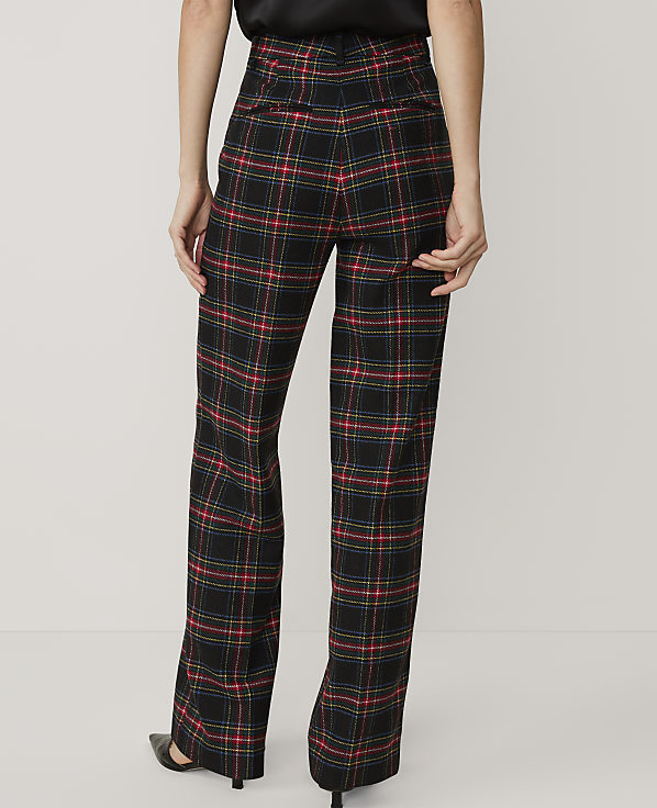A person wearing black, red, and blue plaid trousers and black heels stands against a plain white background.