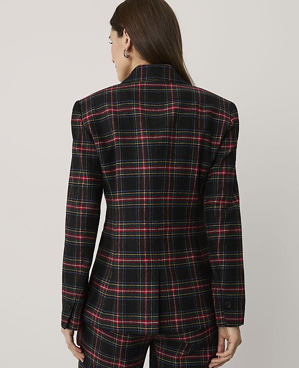 A woman stands with her back to the camera wearing a red, yellow, and blue plaid blazer and matching trousers against a plain light grey background.