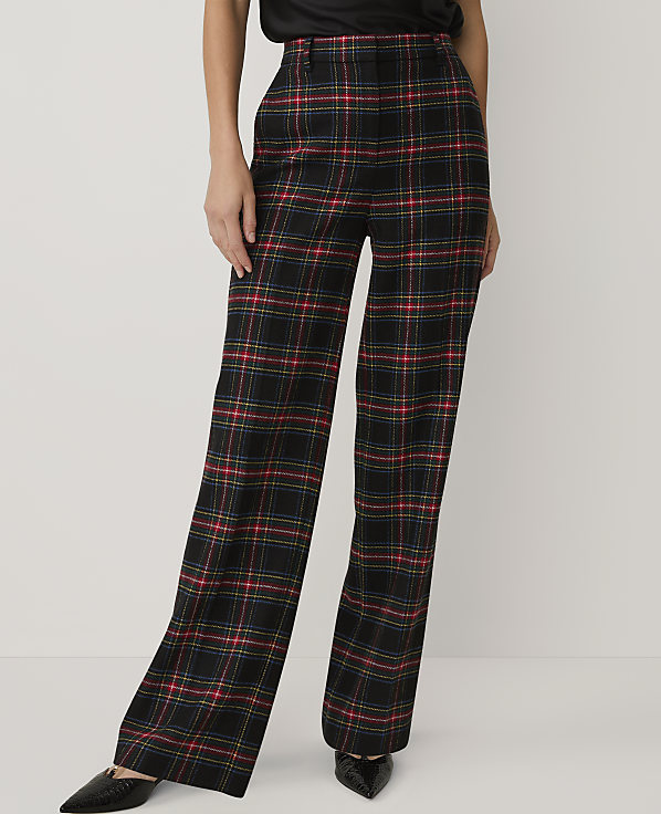 A person wears black, red, and yellow plaid wide-leg trousers and black pointed shoes against a plain white background.