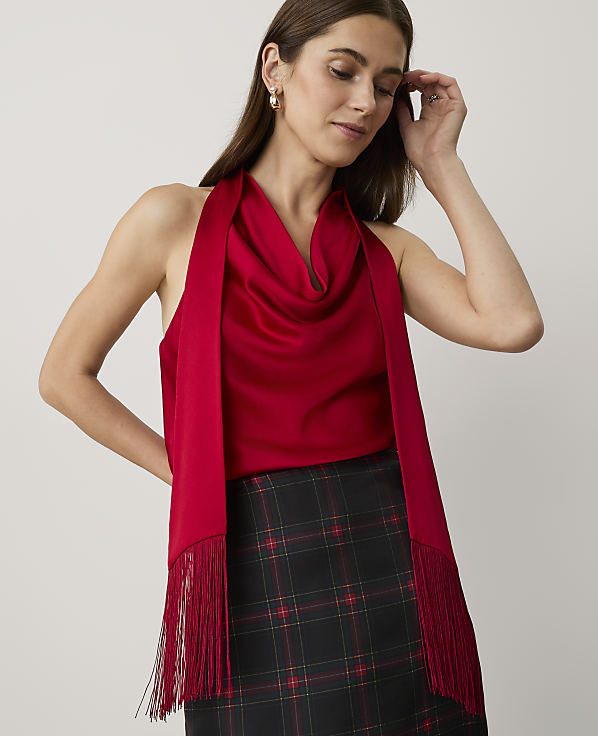 A woman wearing a red satin top and a plaid skirt stands against a plain, light-colored background.