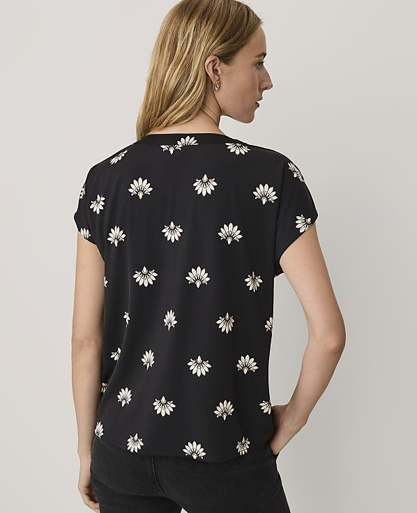 A woman wearing a black floral-print top and black pants stands against a plain white background.