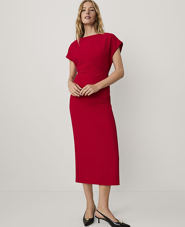 A woman wearing a red midi dress and black heels stands against a plain white background.