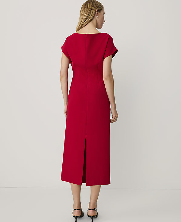 A woman wearing a red midi dress and black heels stands with her back to the camera against a plain white background.