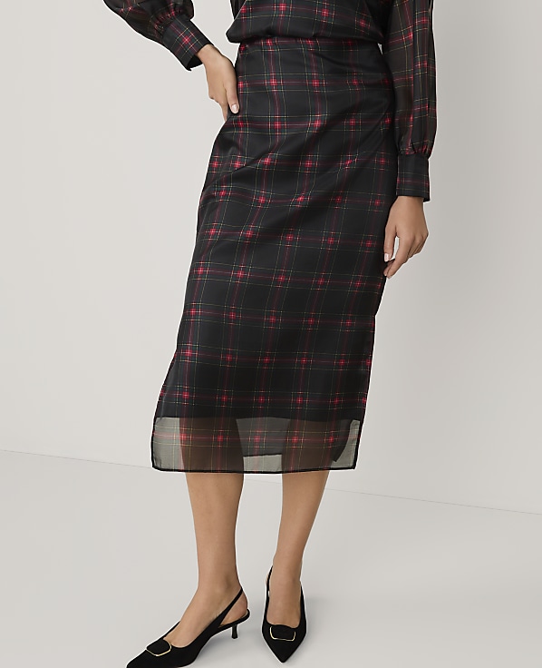 A person wearing a black and red plaid midi skirt and black heels stands against a plain white background.