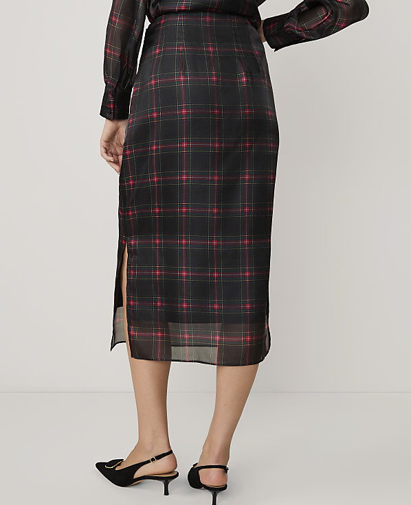 A person wearing a black and red plaid midi skirt and black heels stands against a plain white background.