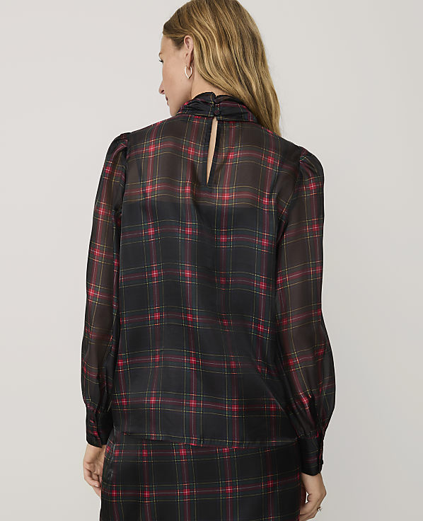 A woman wearing a black and red plaid blouse and matching skirt stands against a plain light gray background.