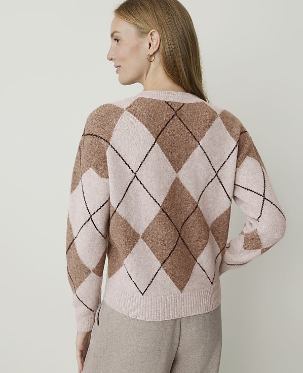 A woman in a tan argyle sweater stands against a plain, light-colored background.