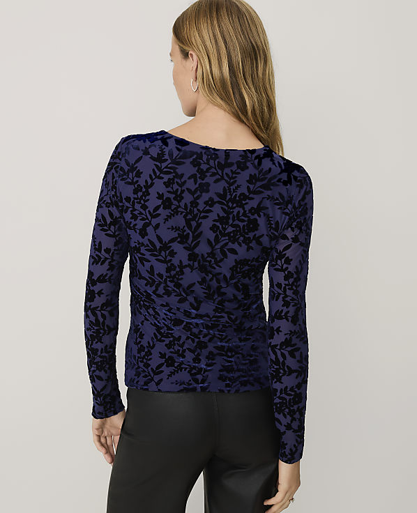 A woman wearing a navy blue floral velvet top and black leather pants stands against a plain light gray background.