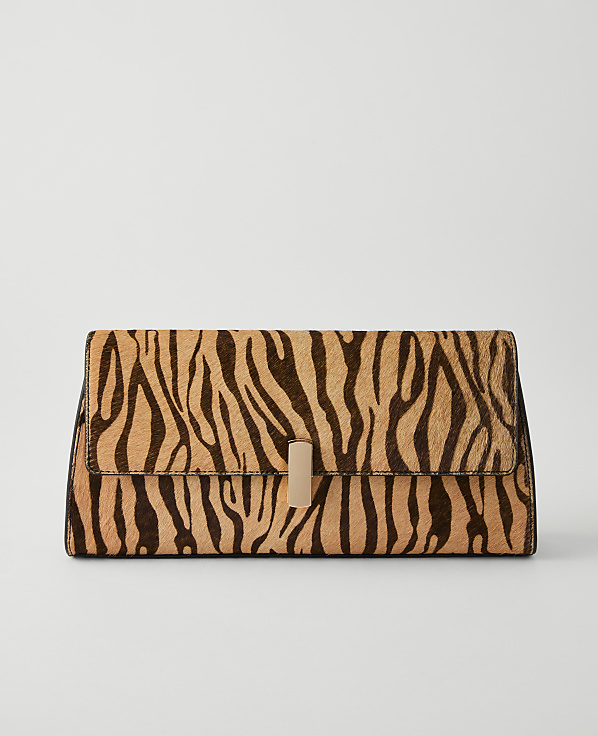A tiger-striped clutch with a gold clasp rests on a plain, light gray background.