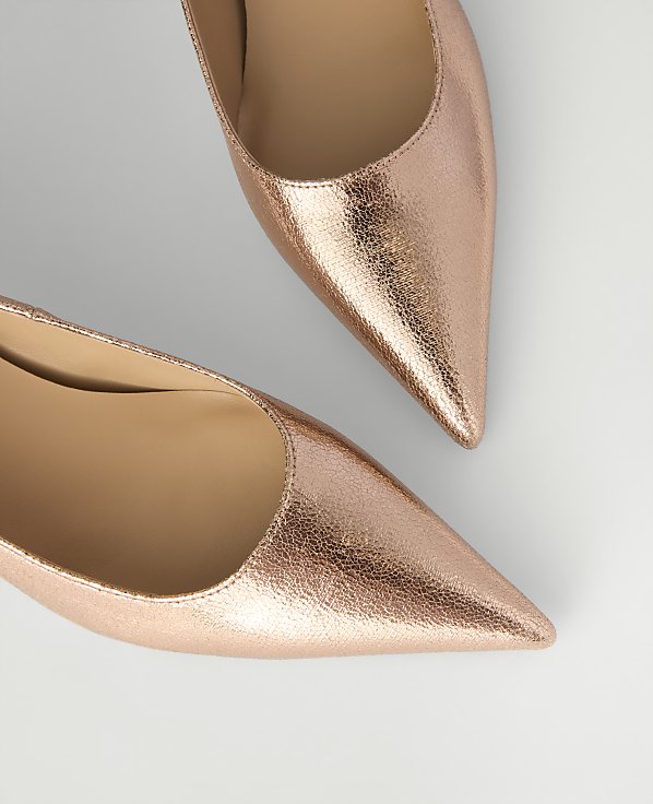 Two metallic rose-gold pointed-toe pumps are positioned diagonally against a plain light gray background.