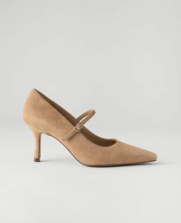 A tan suede pointed-toe pump with a strap sits against a plain, light gray background.