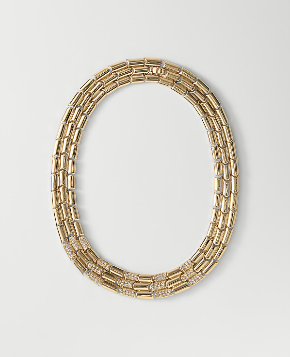 A gold link necklace with diamond accents rests on a plain white background.