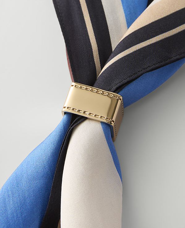 A gold-toned metal ring secures a blue, white, and black striped silk scarf against a plain light gray background.