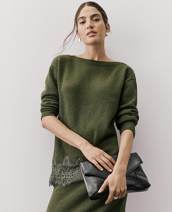 A woman wearing an olive green knit dress with lace detailing holds a black clutch against a plain white background.