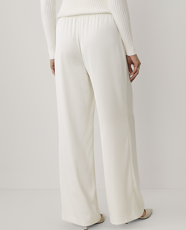 A person wears wide-leg white trousers and a white sweater against a plain, light-colored background.