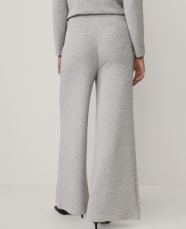 A person stands with their back to the camera wearing grey wide-leg trousers and a matching top against a plain white background.