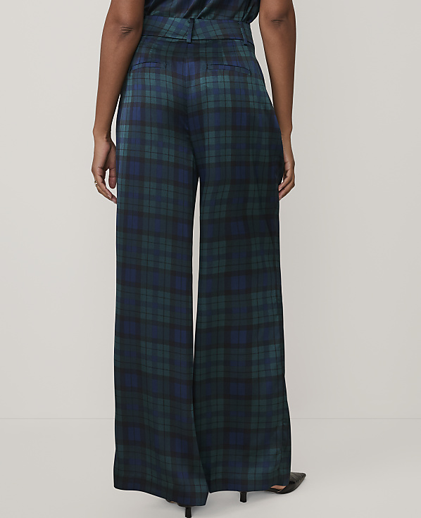 A person stands facing away from the camera wearing wide-leg, dark green and blue plaid trousers against a plain white background.
