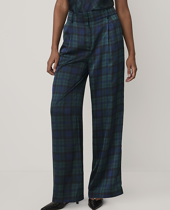A person wears wide-leg, dark green and blue plaid trousers and black pointed shoes against a plain, light-colored background.