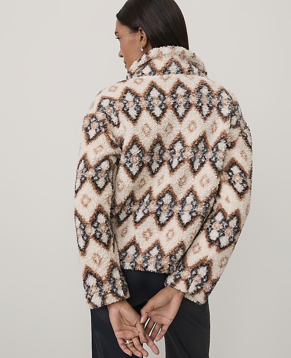 A woman wearing a patterned beige and brown fuzzy jacket stands with her back to the camera against a plain light gray background.