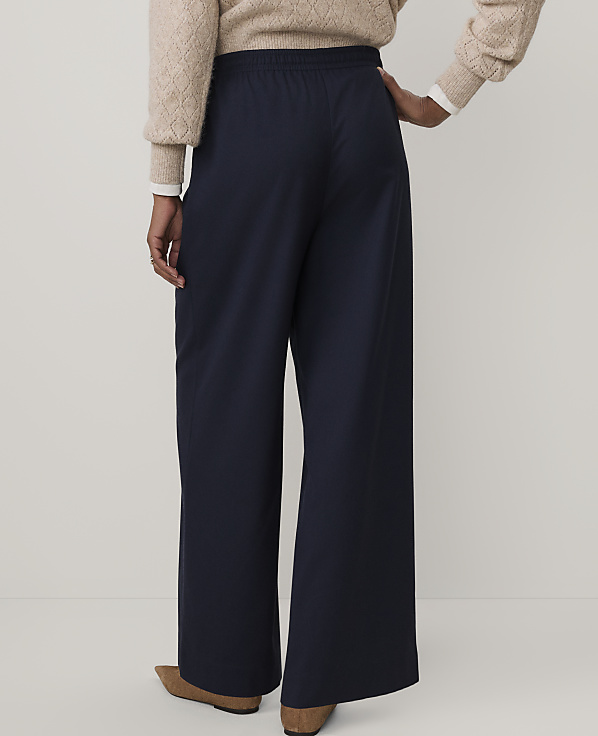 A person wearing a beige sweater and wide-leg navy blue trousers stands against a plain white background.