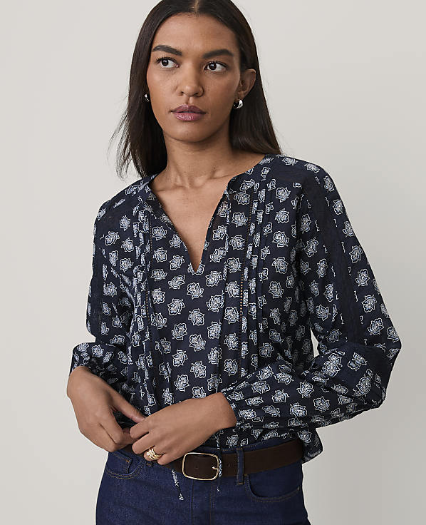 A woman wearing a navy blue floral print blouse and blue jeans stands against a plain, light-colored background.