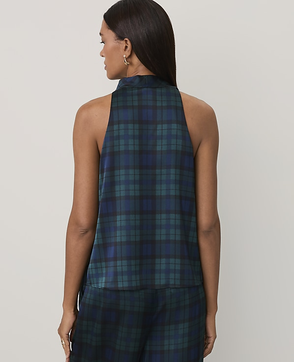A woman wearing a dark green and blue plaid sleeveless top and matching pants stands against a plain, light-colored background.