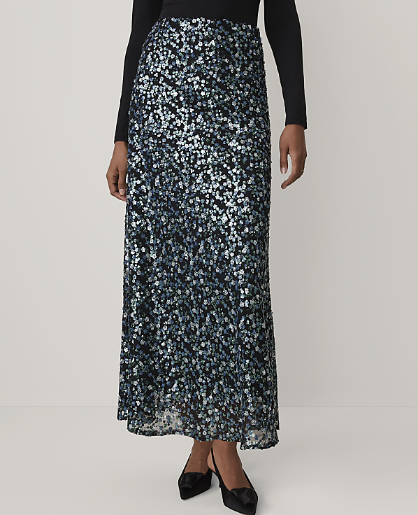 A person wears a long, shimmering blue and silver sequined skirt and a black top against a plain, light-colored background.