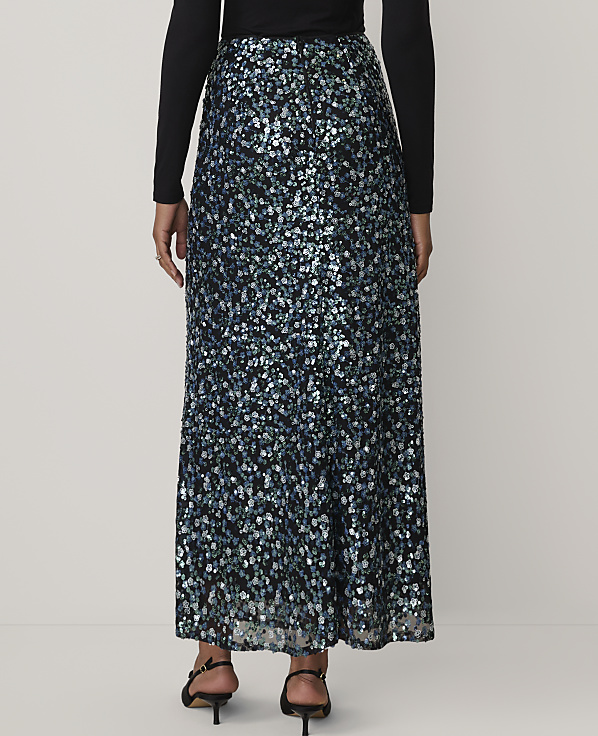 A person wearing a black long-sleeved top and a shimmering blue and silver sequined maxi skirt stands against a plain white background.