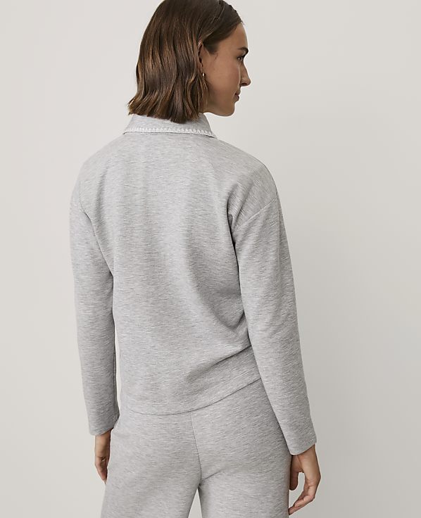 A woman with brown hair wearing a grey matching sweatshirt and pants set stands against a plain white background.