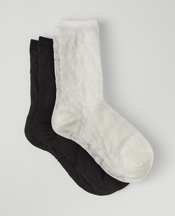 A white sock rests on top of two black socks against a plain light gray background.