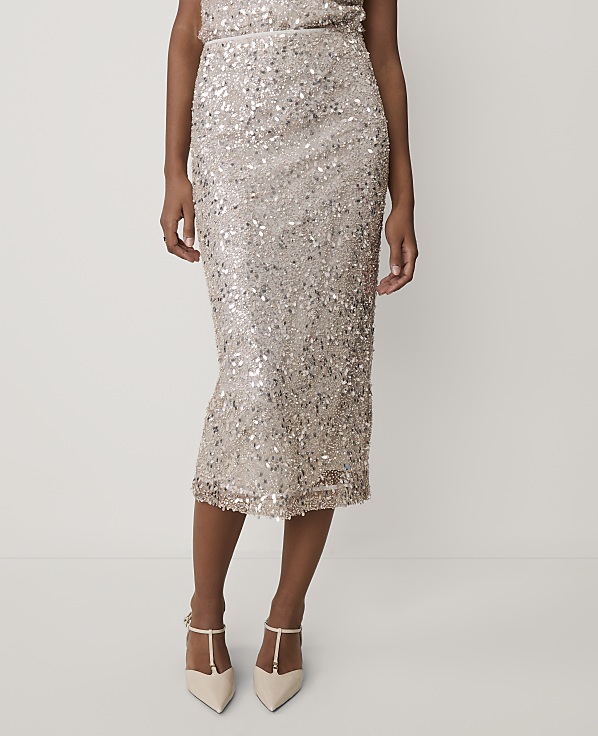 A person wearing a shimmering gold sequined skirt and pointed-toe heels stands against a plain, light-colored background.