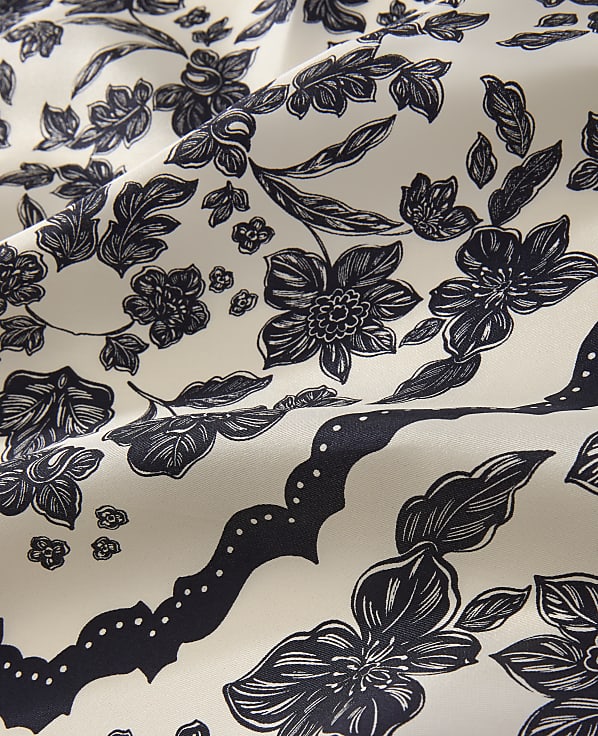 Dark navy floral patterns and scalloped borders are printed across a draped, off-white fabric.