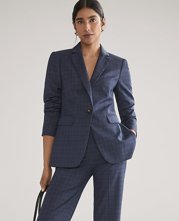 A woman wearing a navy blue plaid suit stands against a plain, light gray background.