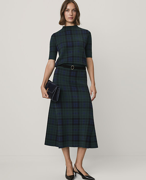 A woman wearing a green and navy plaid matching set with a black belt and heels stands against a plain white background.