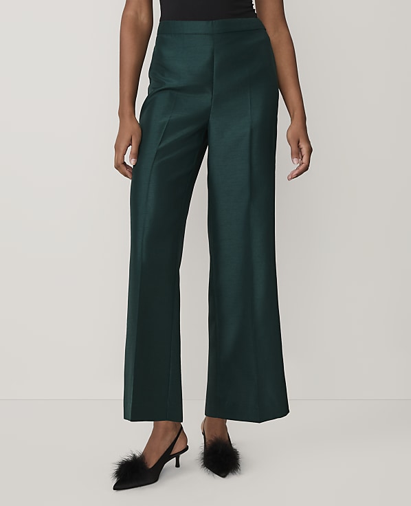 A person wearing dark green wide-leg trousers and black feathered heels stands against a plain white background.