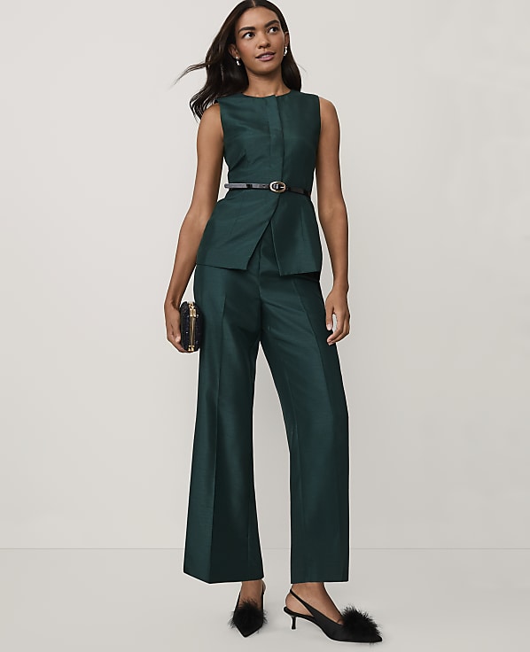 A woman wearing a dark green sleeveless suit and black heels stands against a plain white background.