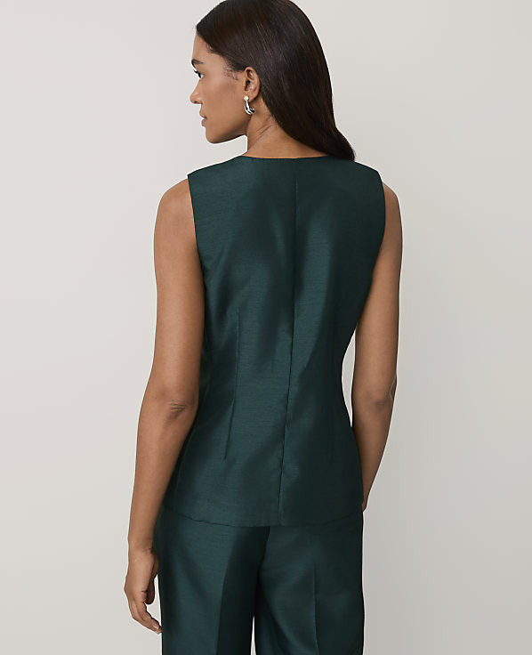 A woman wearing a dark green sleeveless top and matching trousers stands with her back to the camera against a plain light gray background.