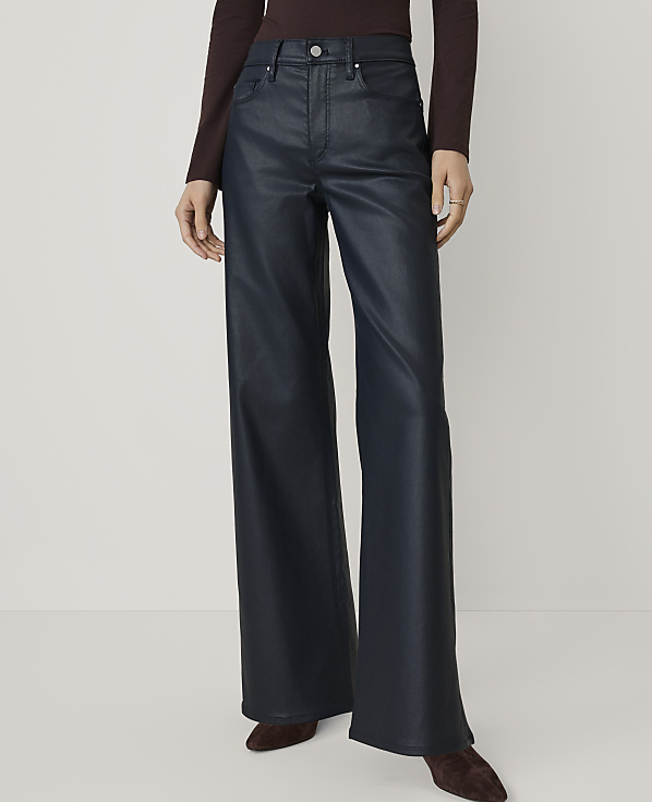 A person wears wide-leg navy faux-leather trousers and a dark burgundy top against a plain, light-colored background.