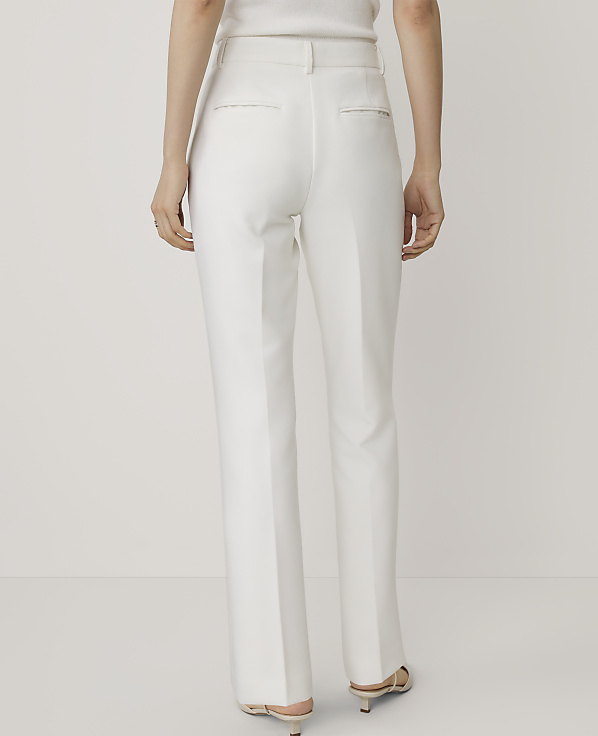 A person stands facing away from the camera wearing white trousers and heels against a plain white background.