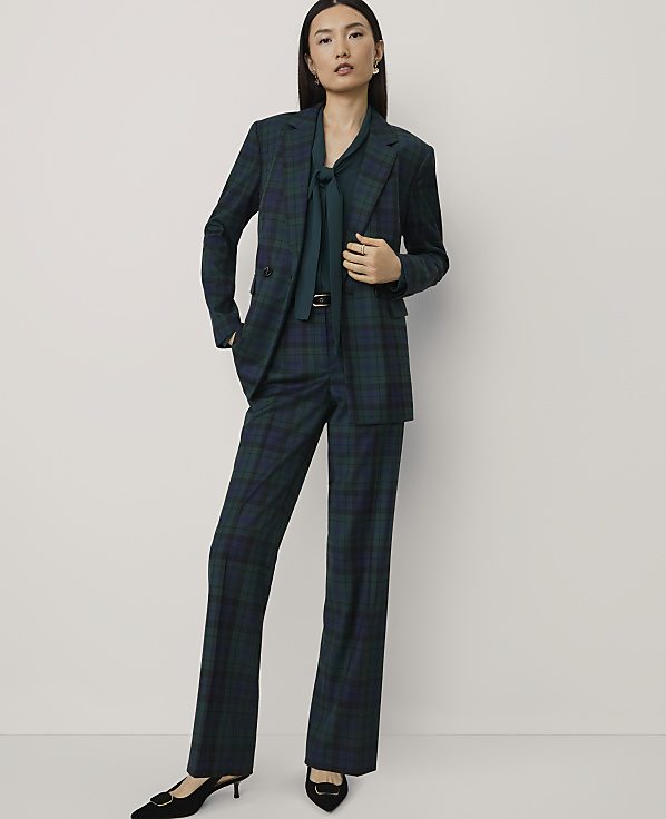 A woman wearing a dark green plaid suit and a matching tie stands against a plain, light-colored background.