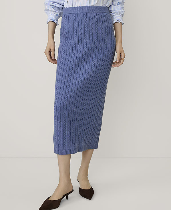 A person wears a blue cable-knit midi skirt and brown heels against a plain, light-colored background.