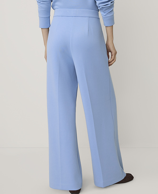 A person wearing light blue wide-leg trousers and a matching top stands against a plain, neutral background.