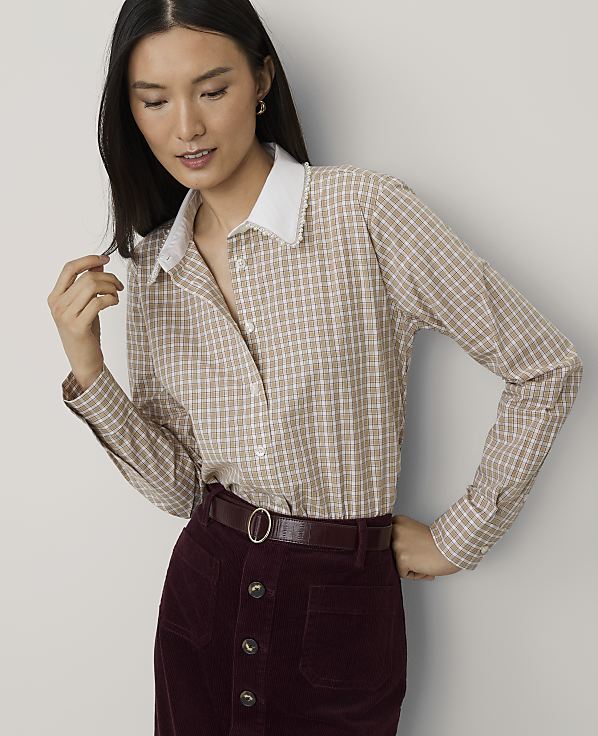 A woman wearing a tan checkered shirt and burgundy corduroy skirt stands against a plain light gray background.