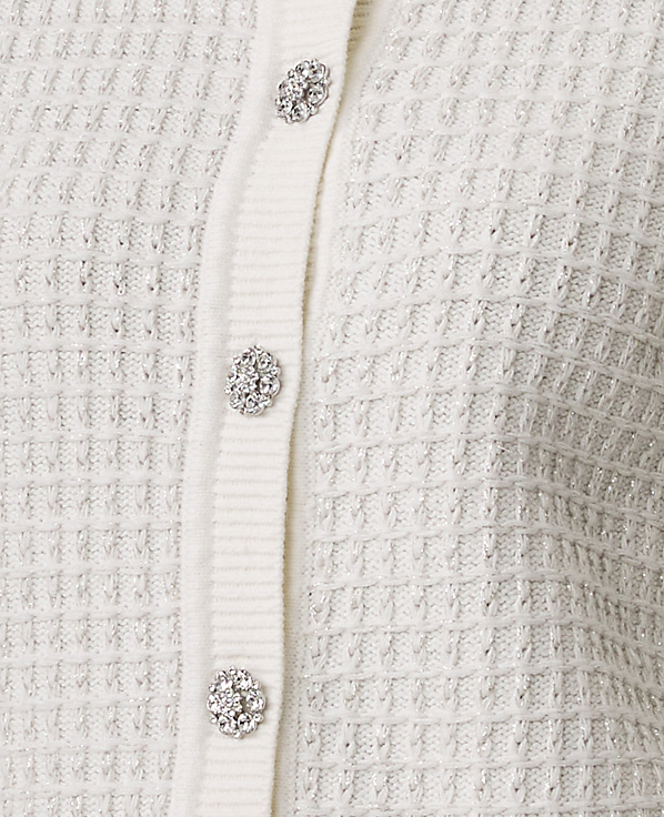Three sparkling rhinestone buttons are aligned vertically on a white textured knit fabric.